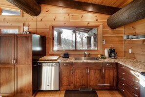 A wooden cabin kitchen with a built-in dishwasher, a window with a view, and a sink.