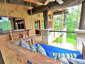 A wooden cabin with a bed, a dining area, and a view of the forest.