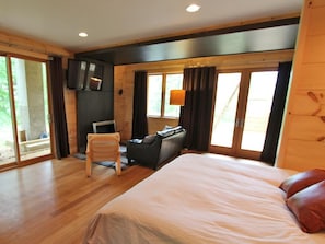 A bedroom with a large bed, a desk with a chair, a television, and a window with curtains.