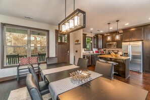 A modern kitchen with dark wood cabinets, stainless steel appliances, and a dining area with a table and chairs. - 3BR amazing view, hot tub, modern luxury sleeps 6 + railroad and rafting tix free (Bryson City)