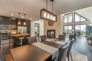 A modern kitchen with built-in appliances, a dining area with a long table, and a large window overlooking a scenic view. - 3BR amazing view, hot tub, modern luxury sleeps 6 + railroad and rafting tix free (Bryson City)