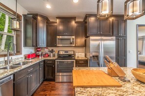 A modern kitchen with dark cabinetry, stainless steel appliances, a granite countertop, and a wooden cutting board. - 3BR amazing view, hot tub, modern luxury sleeps 6 + railroad and rafting tix free (Bryson City)