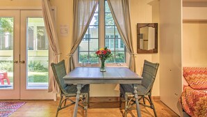 A dining area with a table and chairs, a window with curtains, and a view of greenery outside. - Quiet Saugatuck Studio w/ Patio - Walk to Dtwn! (Saugatuck)