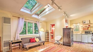 A cozy living room with a sofa, a wooden table, and a patterned rug. There are skylights above the sofa and a kitchen area with cabinets and a microwave. - Quiet Saugatuck Studio w/ Patio - Walk to Dtwn! (Saugatuck)
