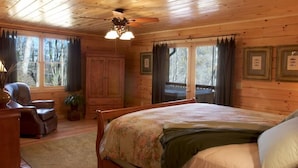 A wooden cabin bedroom with a bed, a chair, a desk, and a ceiling fan.