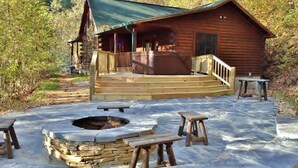 A log cabin with a porch and outdoor seating area, including a fire pit and picnic tables.