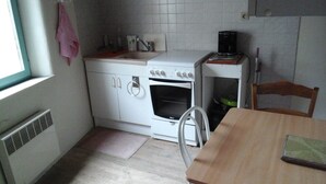 Een compacte keuken met witte kasten, een witte kookplaat, een spoelbak en een klein tafeltje.