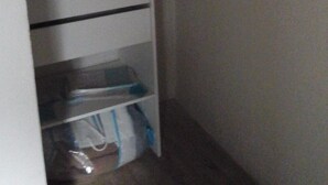 Een opslagruimte met planken, gevuld met opgevouwen kleding en een plastic bak.