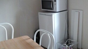 Een kleine keuken met een houten tafel en stoelen, een magnetron en een koelkast.