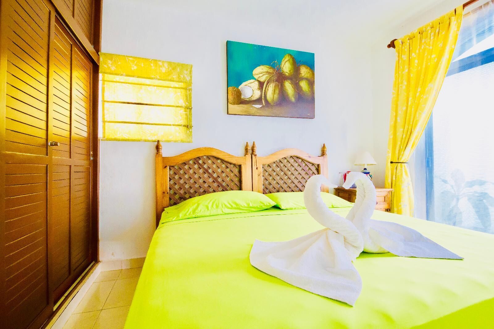 A hotel room with a bed, a wooden headboard, a painting of coconuts, and a towel shaped like a swan.