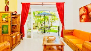 A room with a wooden cabinet, a wooden table, an orange sofa, and a view of an outdoor patio with a table and chairs. - Dolce Vita Caribe Superior Double Room with Pool – Self Check-in - Playacar (Playa del Carmen)