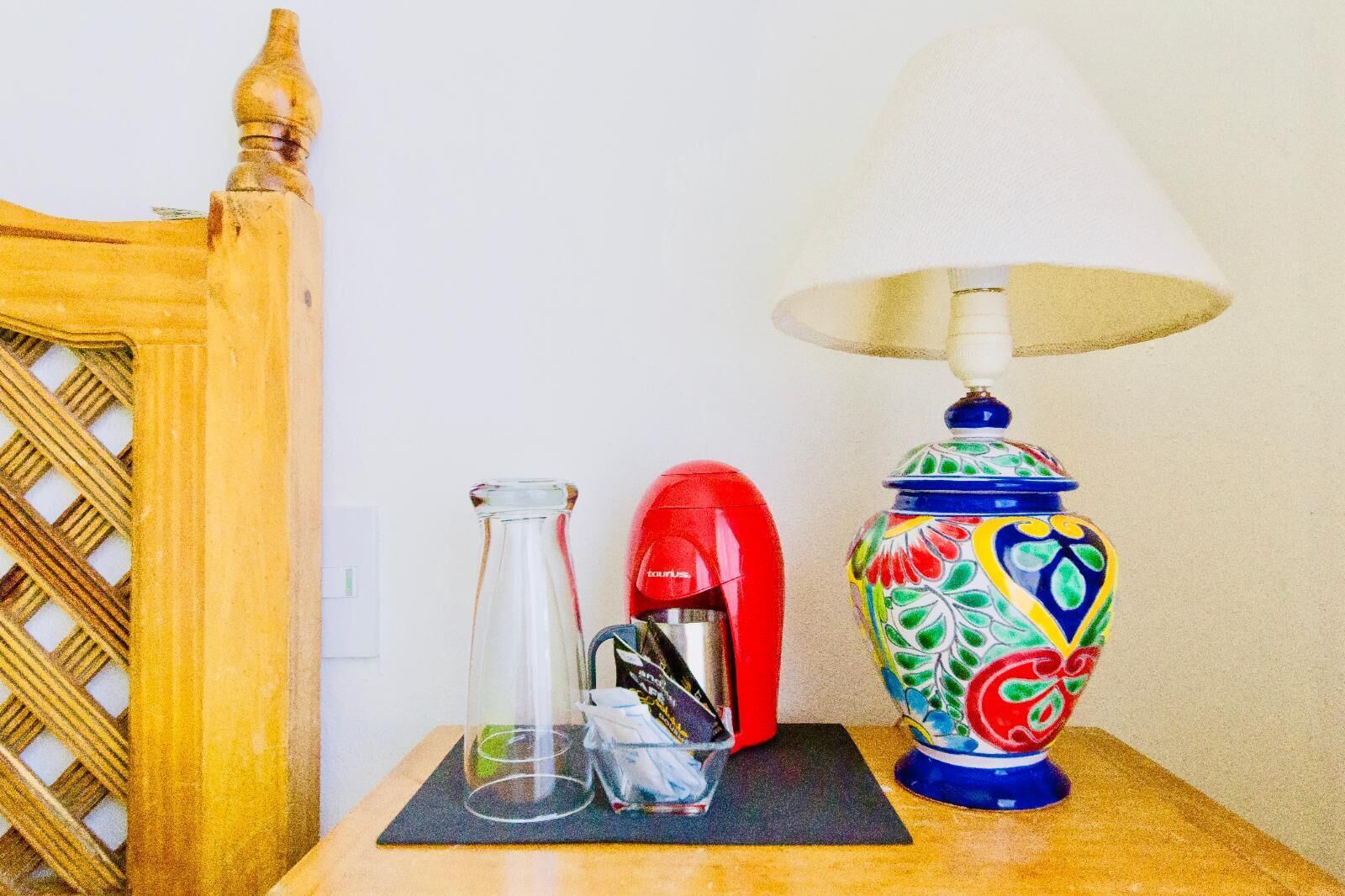 Ein Tisch mit einer farbenfrohen Keramiklampe, einem roten Wasserkocher und einer klaren Glasflasche.