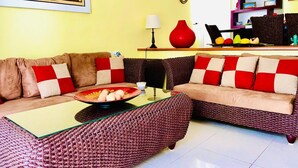 Una sala de estar con un sofá marrón, un cojín a cuadros rojo y blanco, y una mesa de centro tejida.