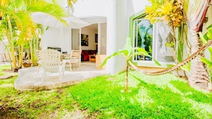 A tropical garden with a patio area, outdoor seating, and a view of the interior.