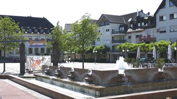 A public square with a fountain, surrounded by multi-story buildings with balconies and a signboard.
