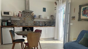 A compact kitchen with a microwave, coffee maker, and a small refrigerator. There is a dining table with chairs and a blue sofa in the living area. - Panoramic view of Marseille and sunset, calm, nature and garden (Marseille)