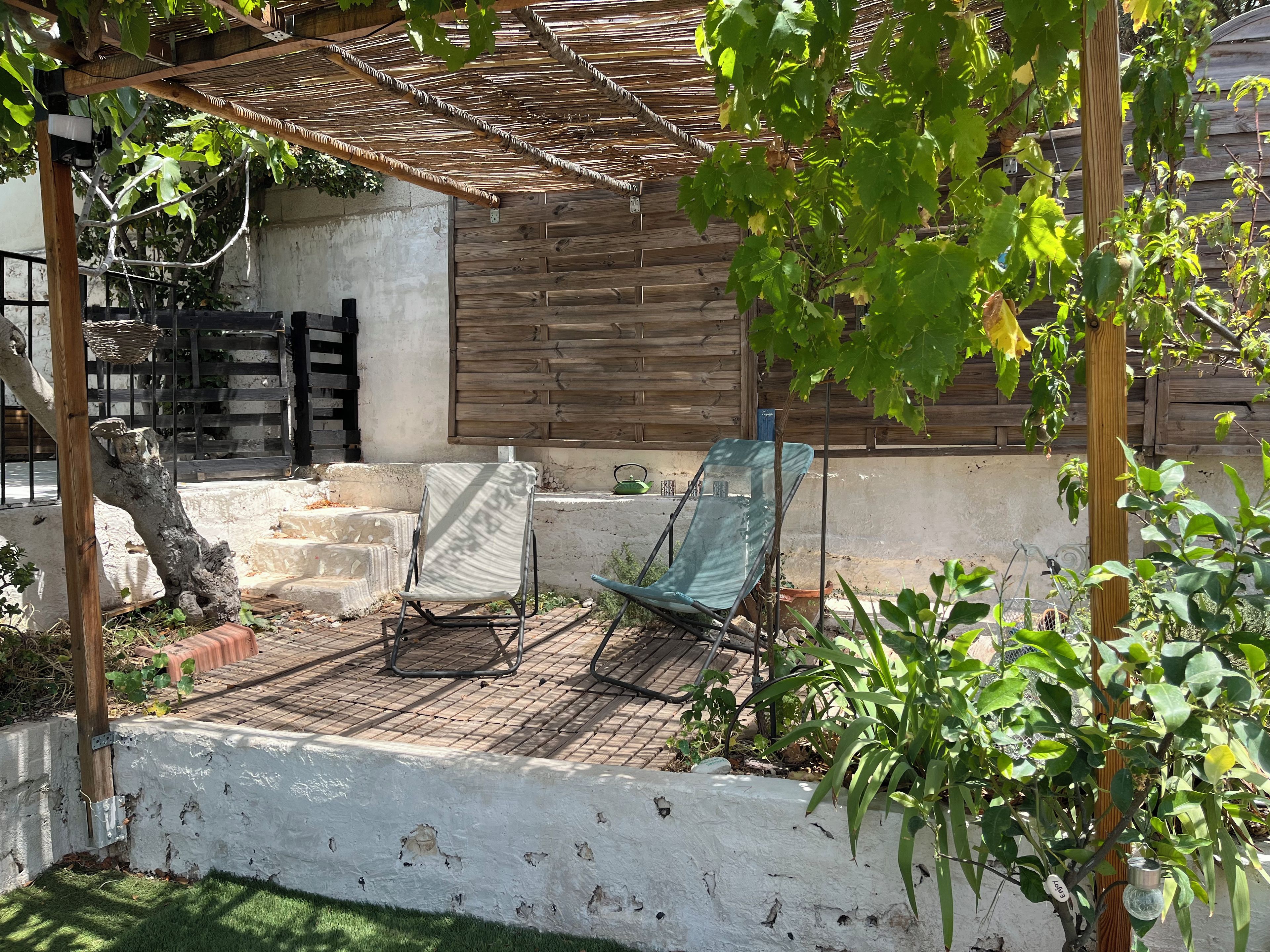 Ein überdachter Patio-Bereich mit einer Pergola, einem Metallstuhl und einem Schaukelstuhl.
