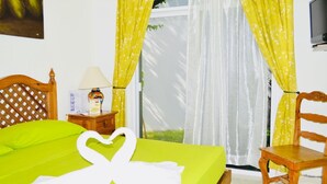 A hotel room with a bed, a wooden chair, a nightstand with a lamp, and curtains. - Superior Villa Playacar – 500 m from the Beach & 5th Avenue (Playa del Carmen)