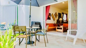 A patio with a table and chairs, a grill, and a sliding glass door leading to an interior space with a sofa and a lamp. - Superior Villa Playacar – 500 m from the Beach & 5th Avenue (Playa del Carmen)