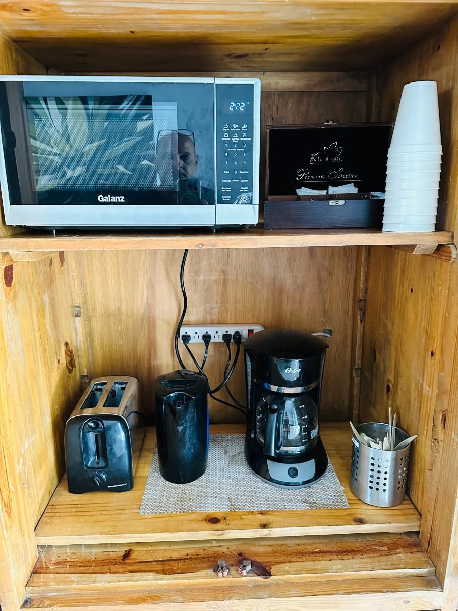 A kitchenette with a microwave, toaster, coffee maker, and a basket of utensils.