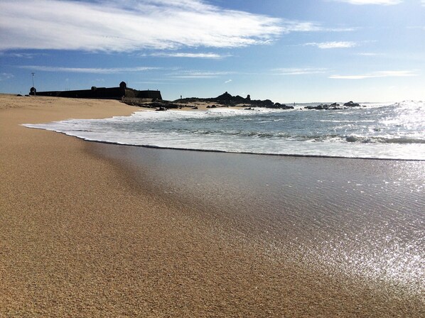 A sandy beach with waves, a clear sky, and rocky outcrops in the distance. - CAPITAL Suite - START NOW! deluxe suites in historic center (Vila do Conde)