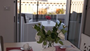 A dining table set for two with a vase of white flowers, a red placemat, and a view of a cityscape and mountains through a large window. - The penthouse view with panoramic view (Palermo)