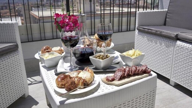 A balcony with wicker furniture, a table with food and drinks, and a view of the city. - The penthouse view with panoramic view (Palermo)