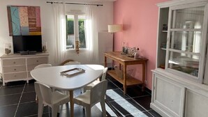 A room with a white dining table, chairs, a TV, a cabinet, and a window with curtains.