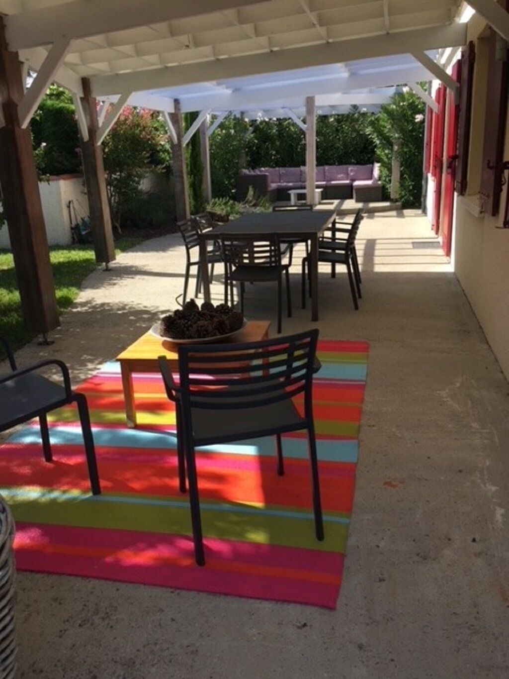 An outdoor patio area with a covered seating area, a table with chairs, and a colorful rug.
