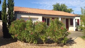 A single-story building with a tiled roof, a front porch, and a garden with flowering plants.