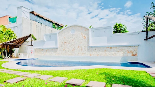 A swimming pool with a stone wall and a thatched roof structure.