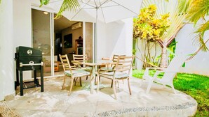 An outdoor patio with a table and chairs, a grill, and a palm tree.