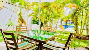 A glass-top table with chairs, surrounded by palm trees and a pool in the background. - Stunning private Comfort villa with pool in Playacar walk to the beach (Playa del Carmen)