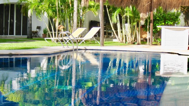 A swimming pool with clear water reflecting palm trees and a thatched-roof structure. - Stunning private Comfort villa with pool in Playacar walk to the beach (Playa del Carmen)