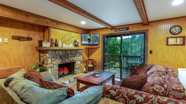 A cozy living room with a stone fireplace, comfortable seating, and a television. - Creekside Condo Walking Distance to Slopes! (Sugar Mountain)