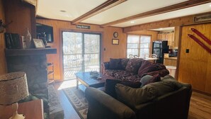 A cozy living room with a fireplace, a sofa, a coffee table, and a television. - Creekside Condo Walking Distance to Slopes! (Sugar Mountain)