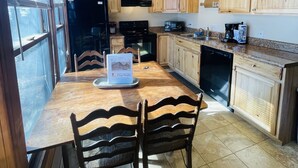 A kitchen with wooden cabinets, a dining table with chairs, and a refrigerator. - Creekside Condo Walking Distance to Slopes! (Sugar Mountain)