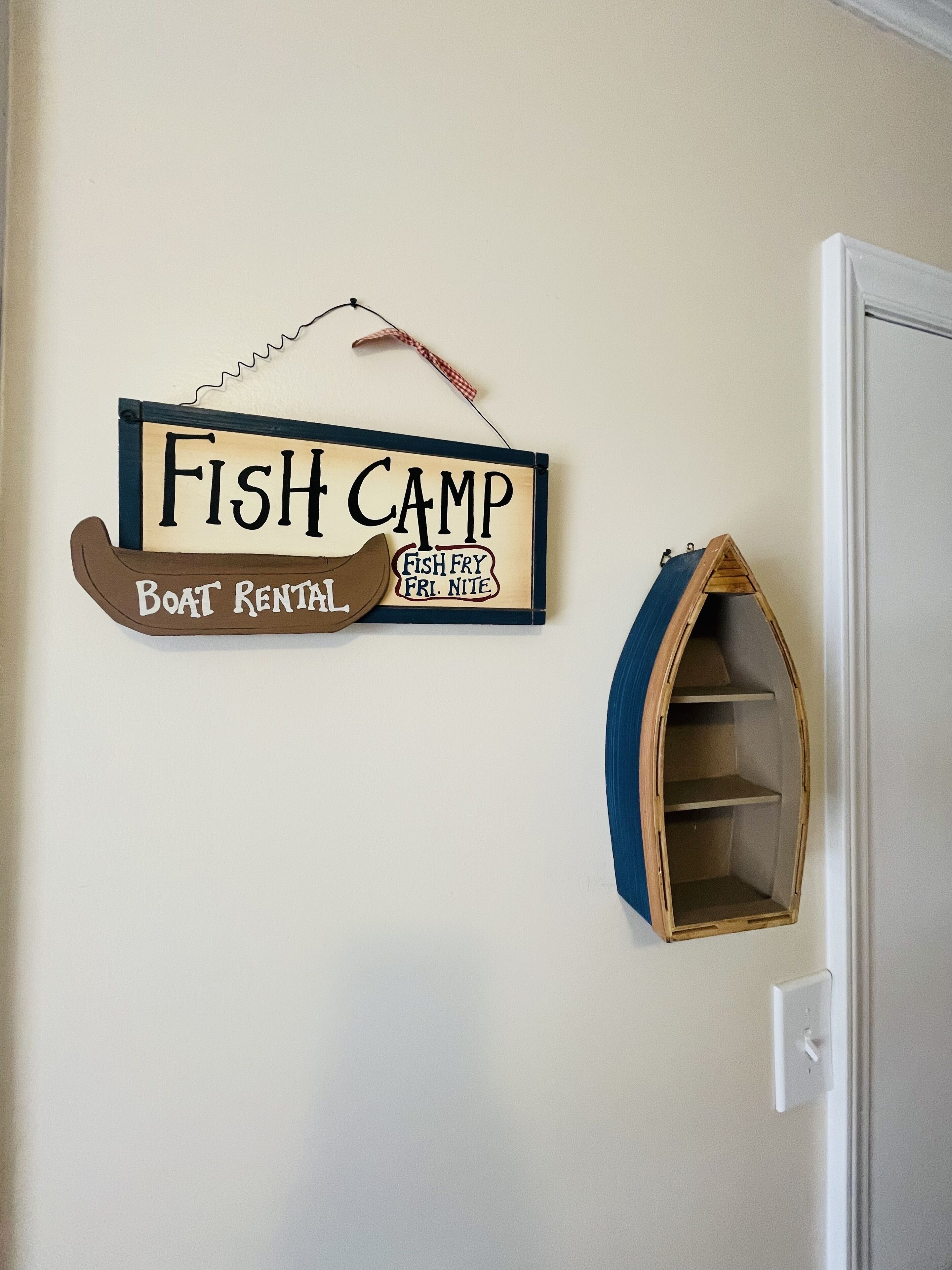 Un letrero en la pared que dice "Fish Camp Boat Rental" con un modelo de barco pequeño debajo.