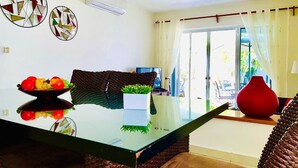 Un comedor con una mesa de vidrio, un frutero y dos obras de arte en la pared.