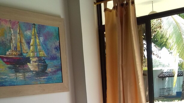 A room with two blue lounge chairs, a wooden table with a hat, a ceiling fan, and a painting of sailboats.