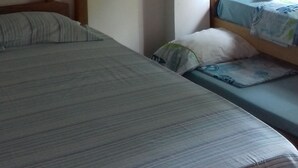 A room with two beds, a wooden ceiling, a window with blue curtains, and a wall-mounted air conditioner.