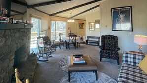 Una sala de estar acogedora con chimenea de piedra, un comedor con mesa y sillas, y una alfombra estampada.