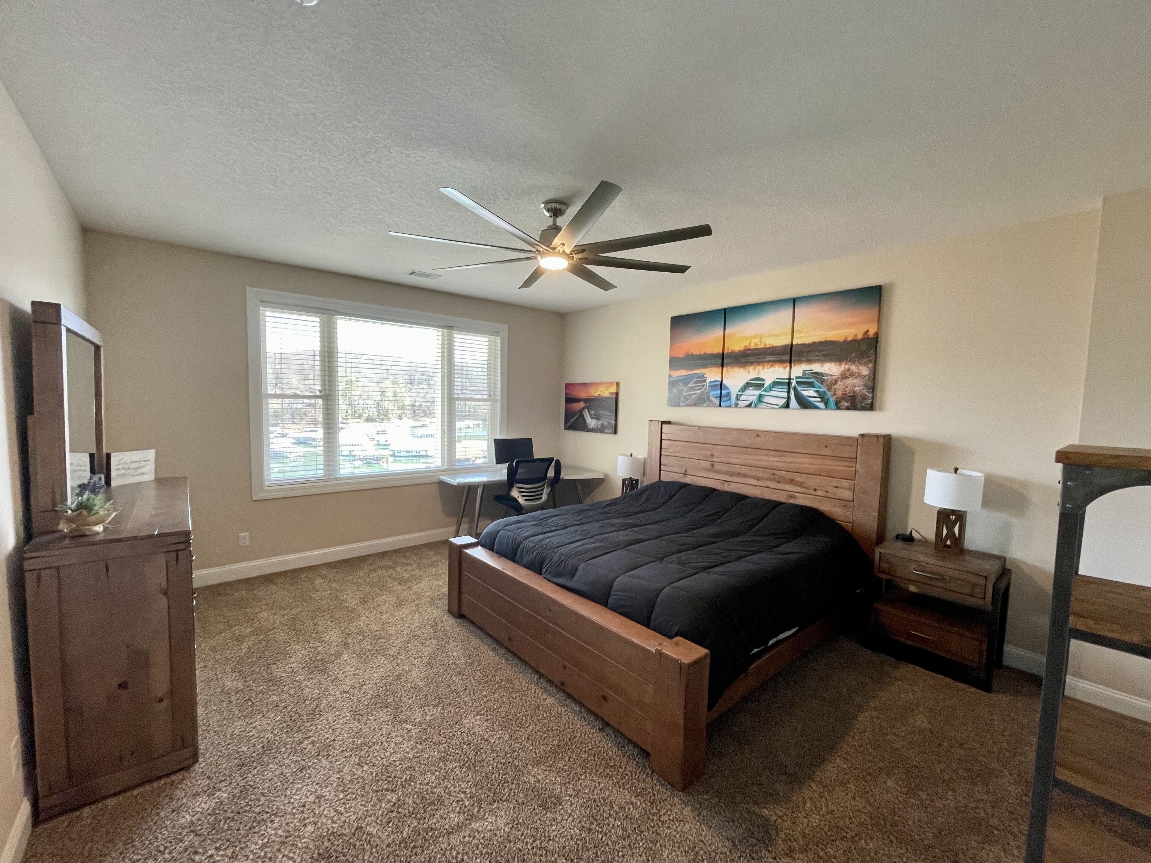 A bedroom with a wooden bed, a ceiling fan, a desk, and a chair.