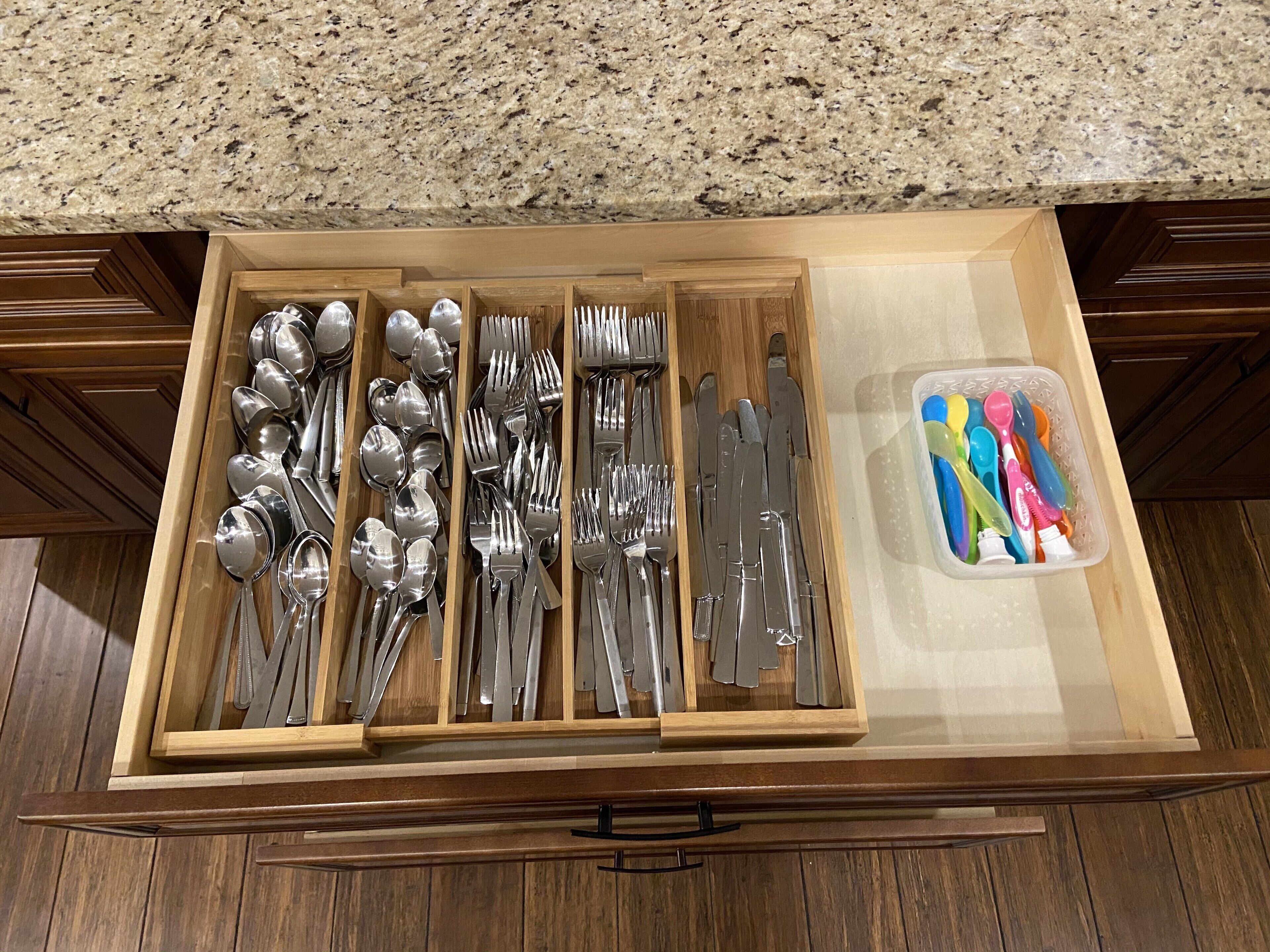 A drawer with utensils and a container of colorful spoons.