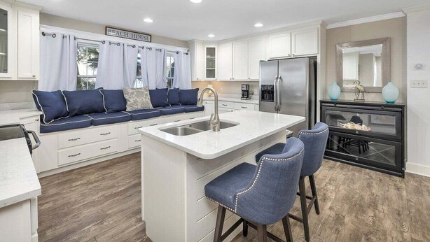 A modern kitchen with white cabinets, a central island with bar stools, a stainless steel refrigerator, and a sign reading "BEACH HOUSE". - The perfect Complex to fit your large group needs! (Saint Simons Island)
