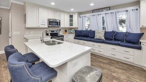 A kitchen with white cabinets, a built-in oven, a microwave, and a sink. There is a blue sofa with cushions and a sign above the windows that reads "Beach House." - The perfect Complex to fit your large group needs! (Saint Simons Island)