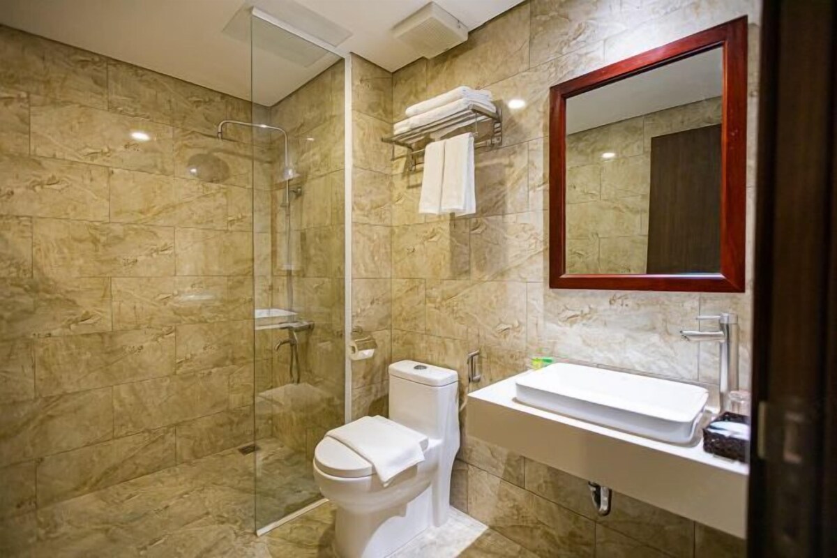A bathroom with a glass-enclosed shower, a toilet, and a sink with a mirror above it.