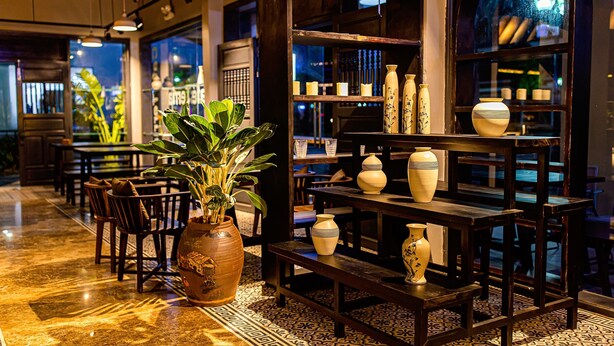 A restaurant interior with a marble floor, wooden furniture, and a variety of decorative vases on shelves. - Bayya Hotel Phu Quoc (Phu Quoc)