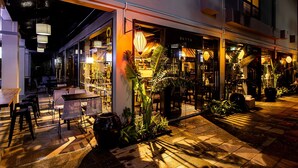 An outdoor seating area with tables and chairs, surrounded by potted plants and a well-lit entrance to a building. - Bayya Hotel Phu Quoc (Phu Quoc)