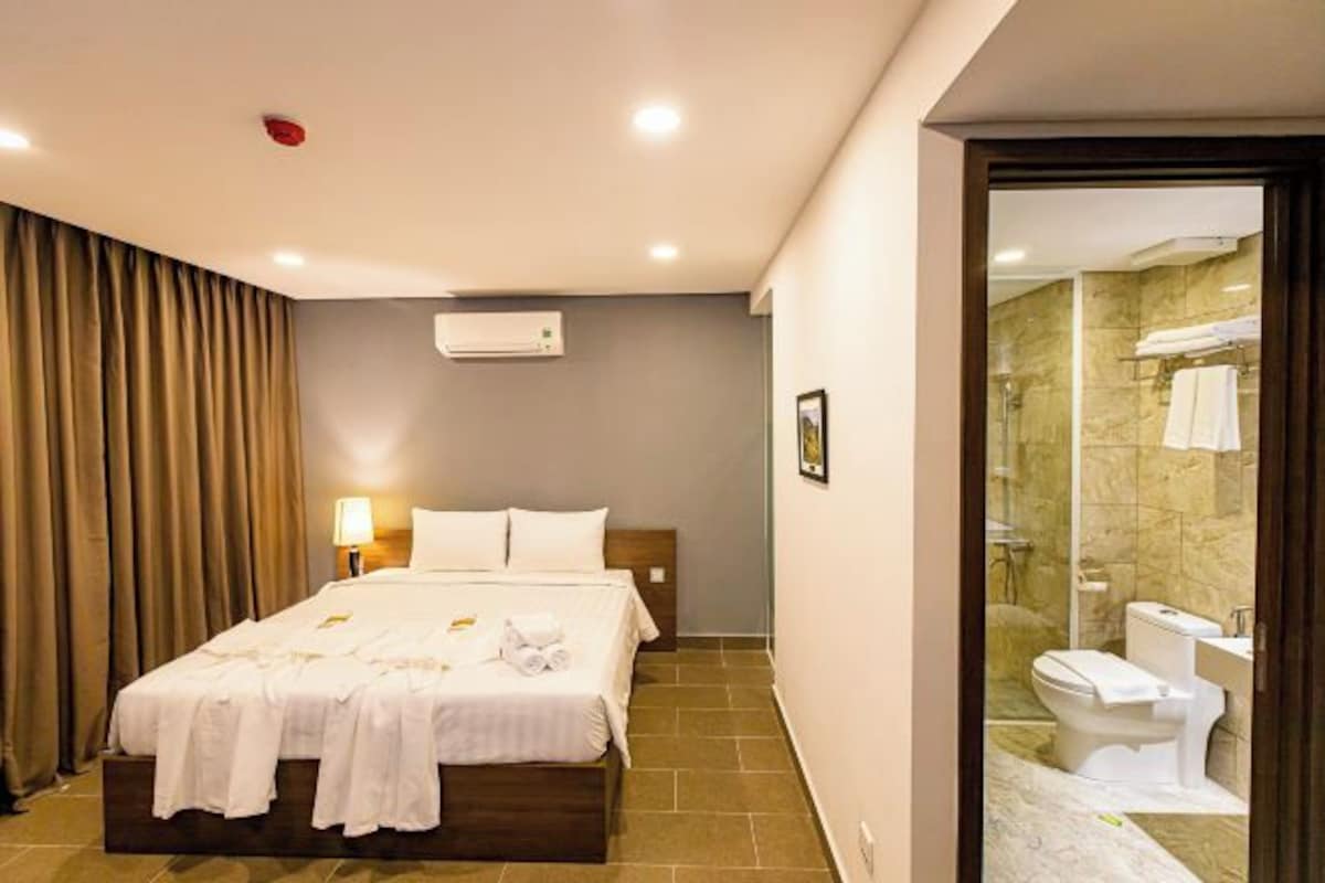 Camera d'albergo con un letto, una lampada da comodino, un condizionatore d'aria, un box doccia con porta in vetro e un WC.